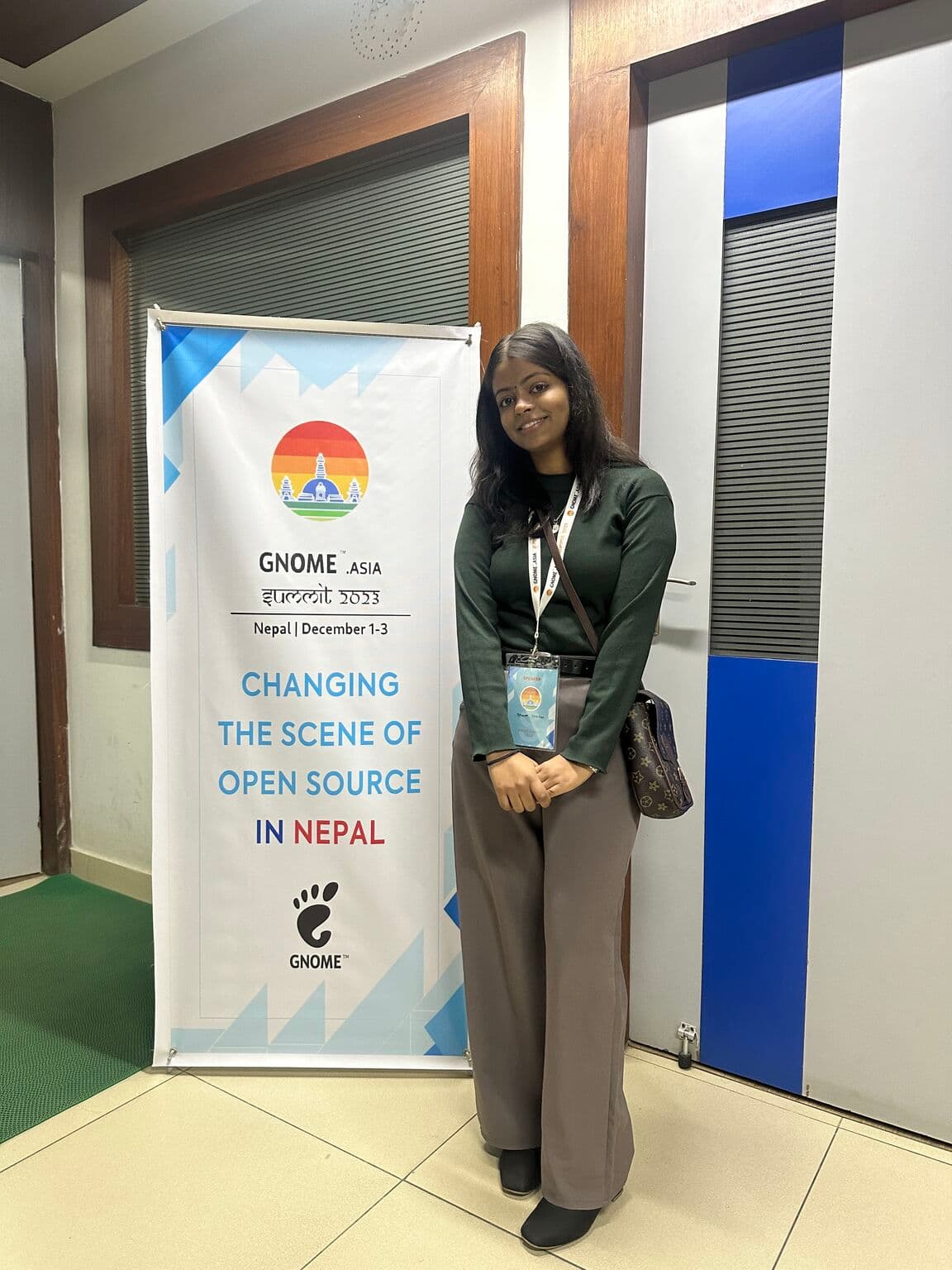 Bhawna standing beside the GNOME Asia Summit 2023 banner in Nepal